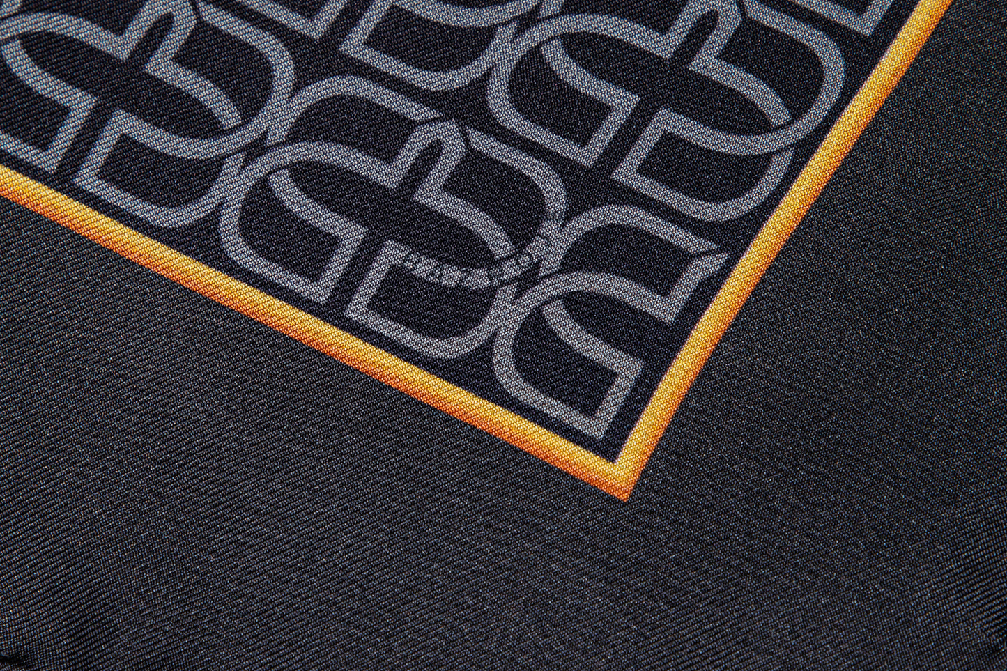 Close-up of a black scarf featuring a repeating gray interlocking monogram pattern and a bright orange border.